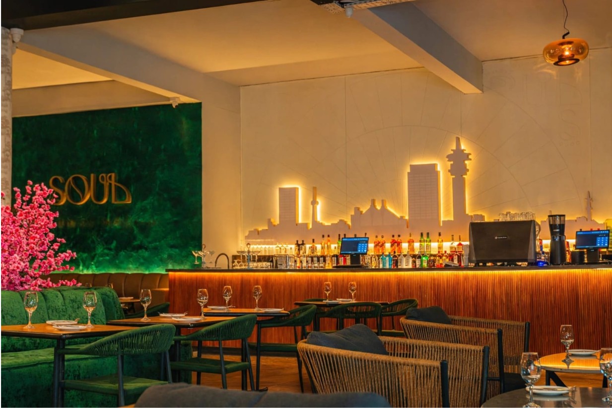 The Soul dining room and bar: gold SOUL letters on a green wall, an illuminated city skyline behind the bar, green velvet seating and set tables